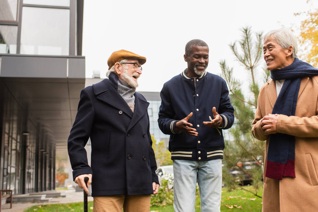 glimlachende Afrikaan amerikaanse man praten met interraciale vrienden op stedelijke straat  - Foto, afbeelding