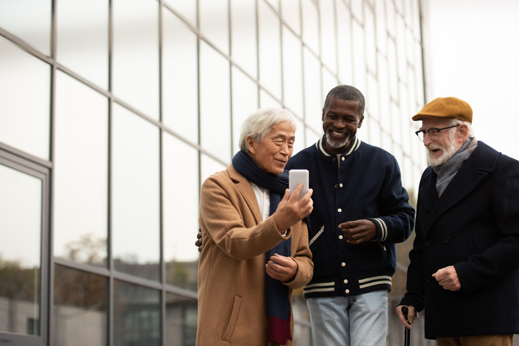 Старший азиат использует смартфон рядом с многонациональными друзьями на городской улице  - Фото, изображение