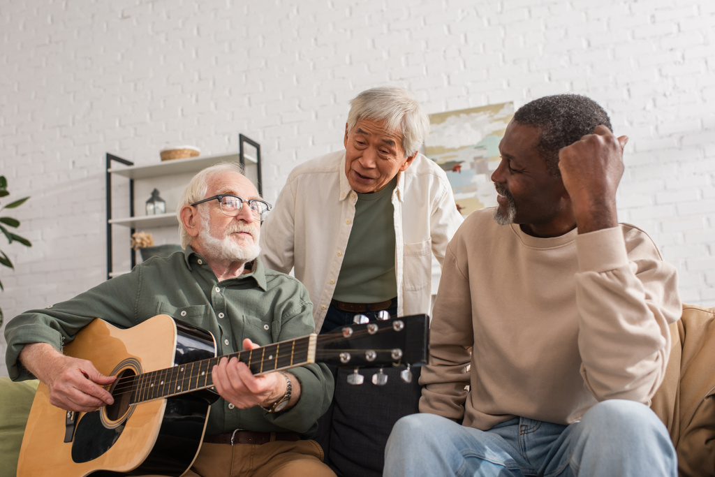 Rotujenväliset eläkeläiset katsovat kaveria, joka soittaa akustista kitaraa kotona  - Valokuva, kuva