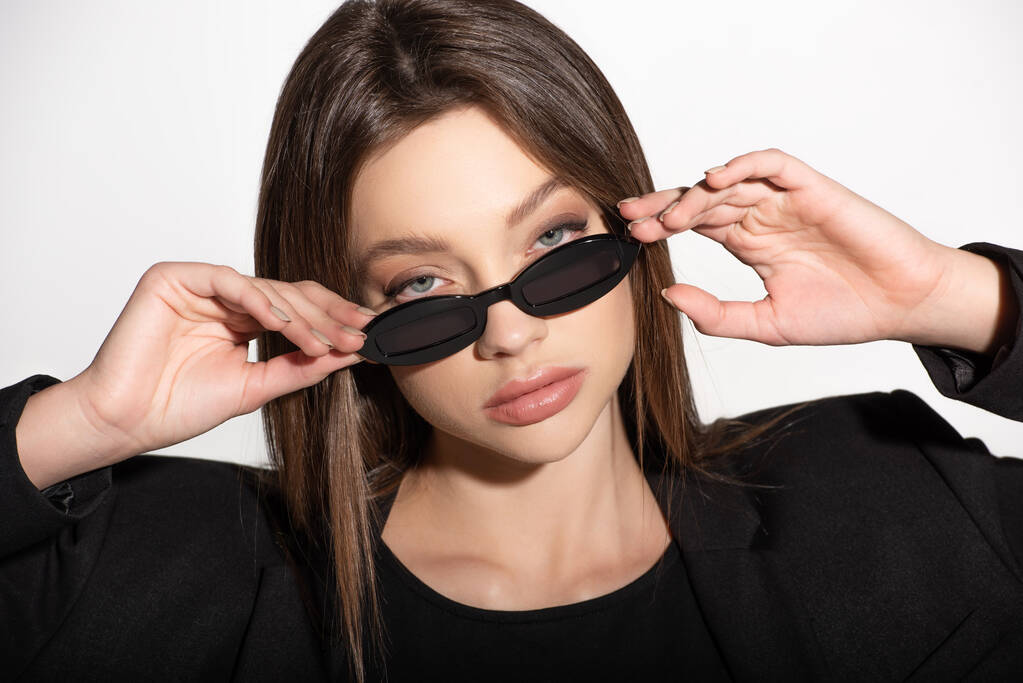 portrait of pretty brunette woman looking at camera over black sunglasses isolated on grey - Photo, Image