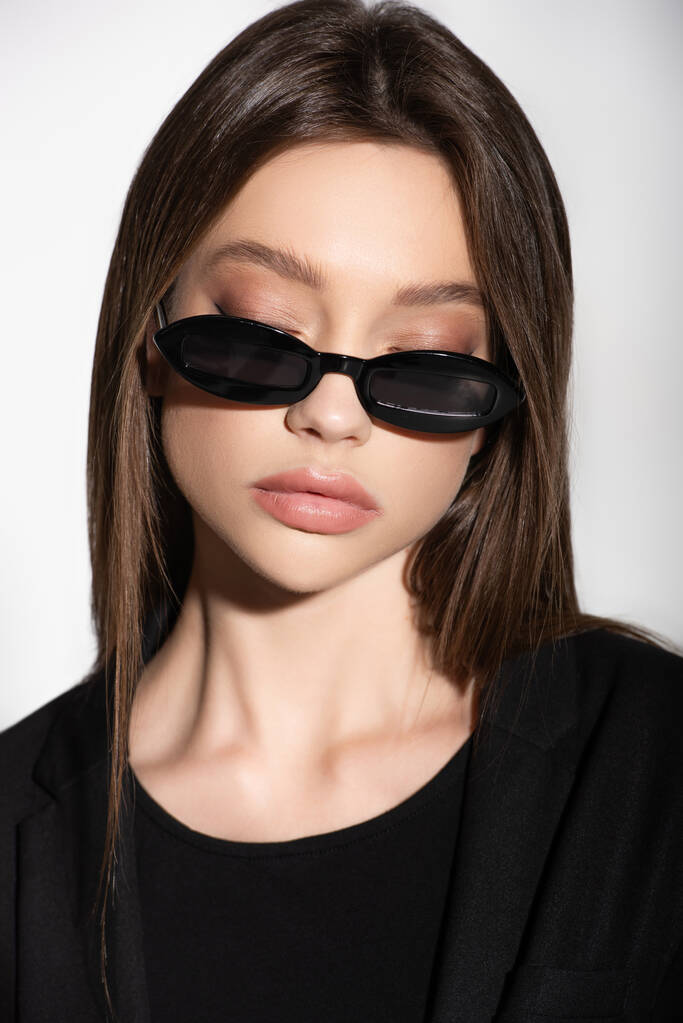 портрет юной брюнетки в черных солнцезащитных очках, изолированных на сером - Фото, изображение
