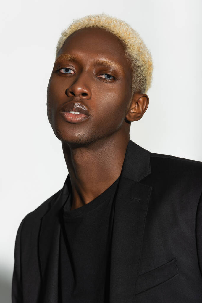 portrait of blonde african american man in black blazer looking at camera isolated on grey - Photo, Image