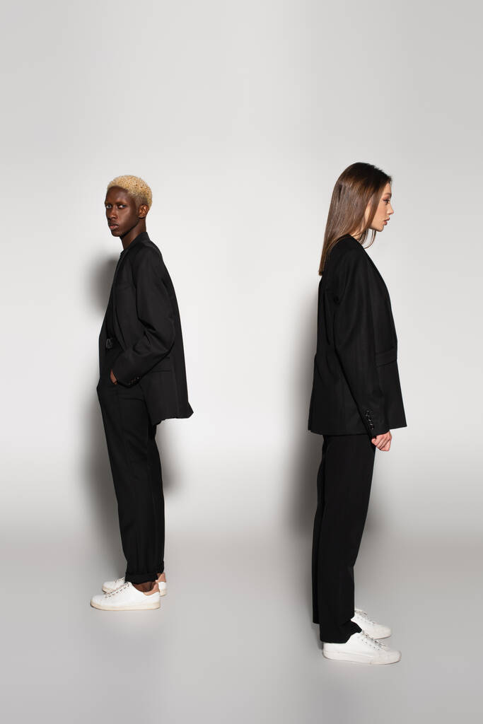 african american man with bleached hair standing with hand in pocket near stylish woman on grey with shadow - Photo, Image