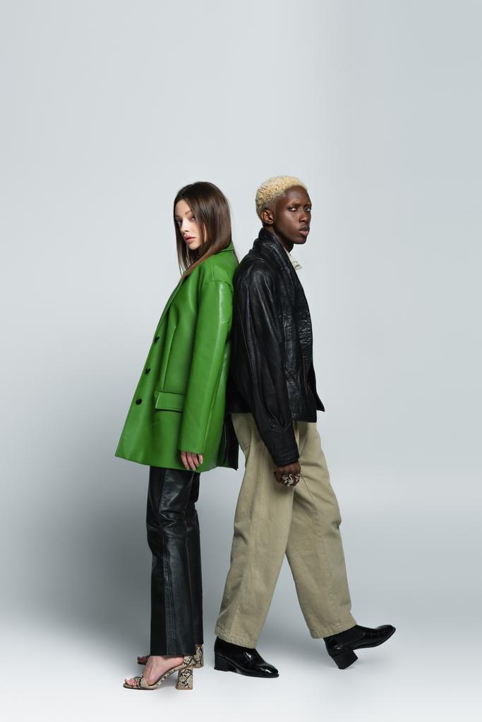 full length view of blonde african american man and brunette woman standing back to back on grey - Photo, Image