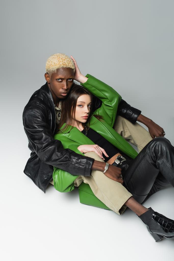 vysoký úhel pohledu bruneta žena a blondýny africký americký muž objímání zatímco sedí na šedé - Fotografie, Obrázek