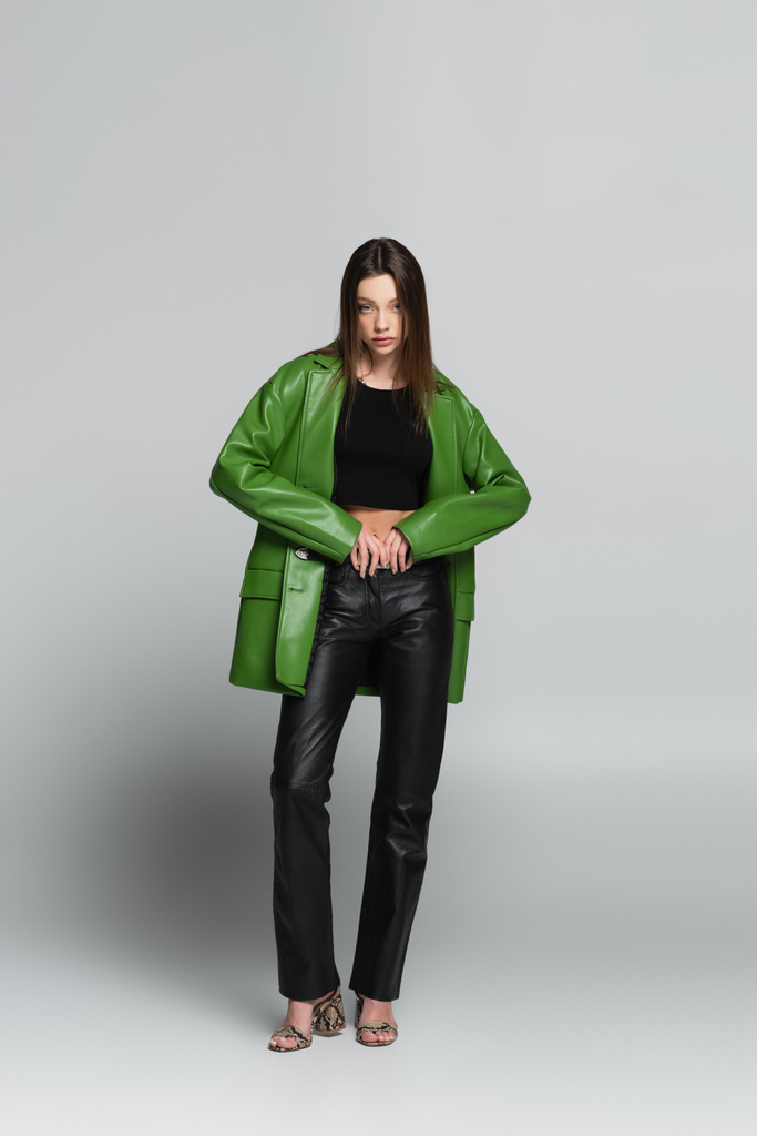 visão de comprimento total da mulher na moda em jaqueta de couro e calças olhando para a câmera no cinza - Foto, Imagem