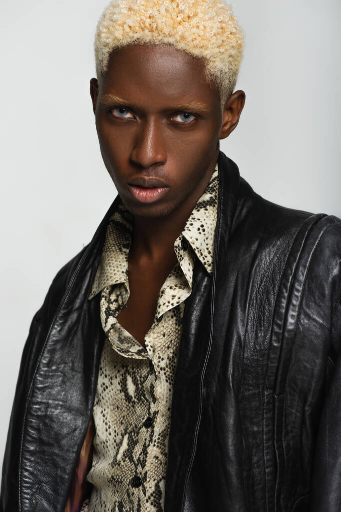 blond homme afro-américain en veste en cuir et chemise imprimé peau de serpent isolé sur gris - Photo, image