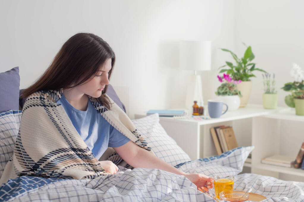 nemocný teen dívka s čajem na posteli v bílém pokoji - Fotografie, Obrázek