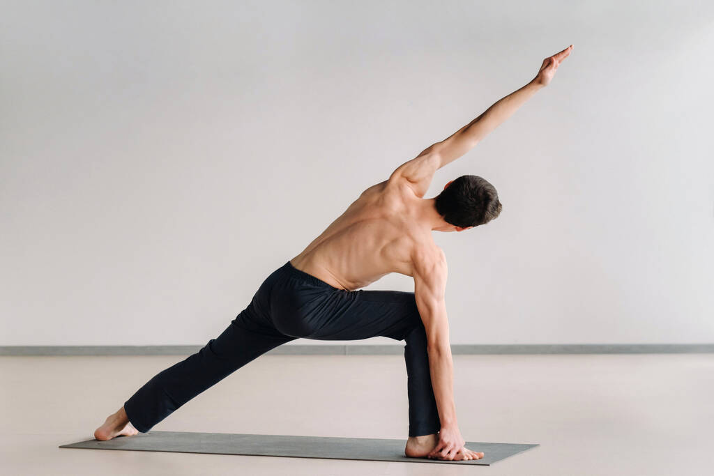 Ein Mann mit nacktem Oberkörper trainiert im Stehen Dehnen im Fitnessstudio. - Foto, Bild