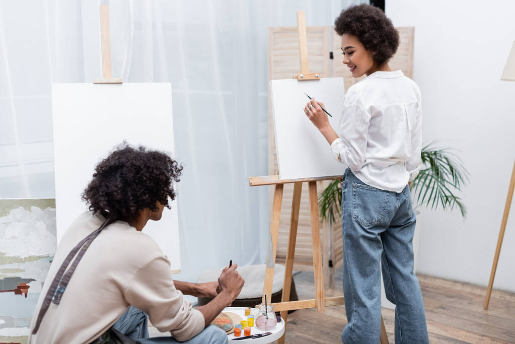 笑顔アフリカ系アメリカ人女性絵画上のキャンバスと見ますボーイフレンドで家  - 写真・画像