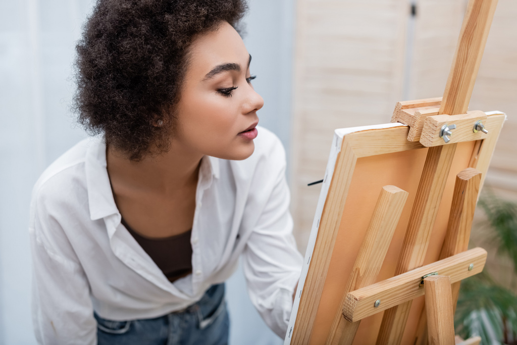 アフリカ系アメリカ人女性が自宅でイーゼルでキャンバスに絵を描く  - 写真・画像