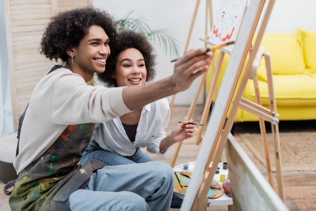 Glückliches junges afrikanisch-amerikanisches Paar malt zu Hause auf Leinwand  - Foto, Bild