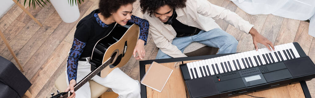 Bovenaanzicht van jong Afrikaans Amerikaans echtpaar dat thuis muziekinstrumenten bespeelt, spandoek  - Foto, afbeelding