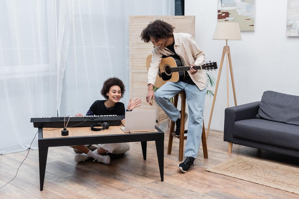 Couple afro-américain positif avec instruments de musique ayant appel vidéo sur ordinateur portable à la maison  - Photo, image