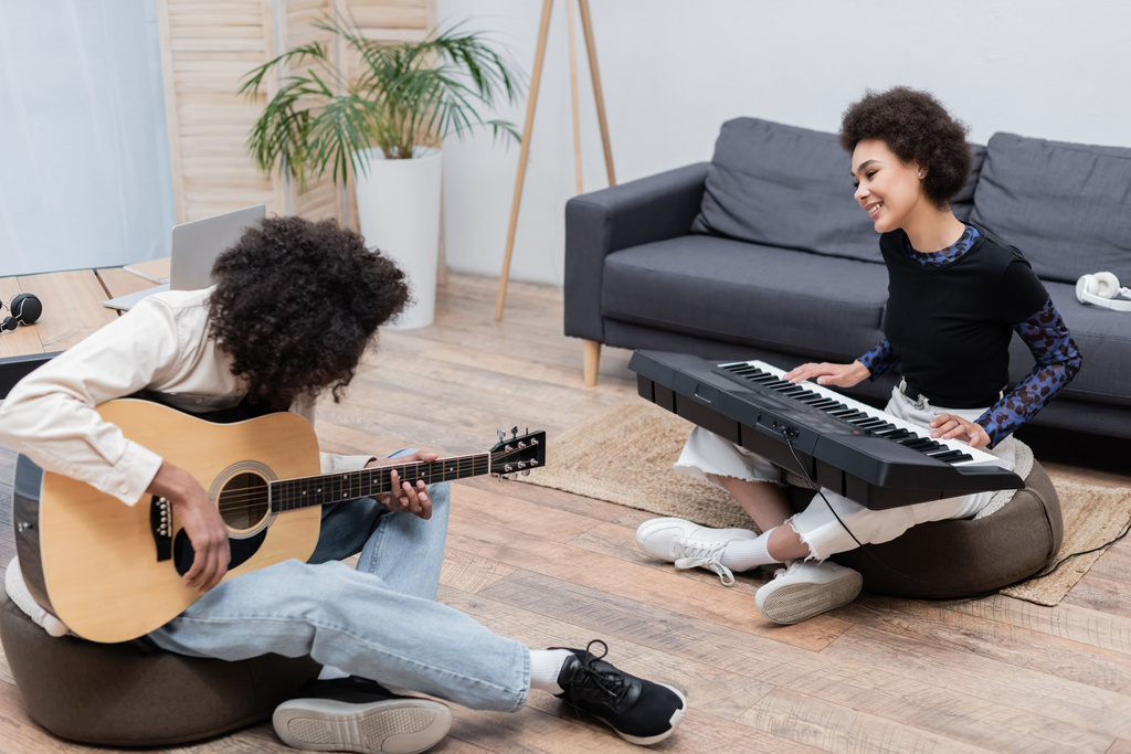 笑顔アフリカ系アメリカ人ミュージシャン再生シンセサイザー近くボーイフレンドとともにアコースティックギターで自宅  - 写真・画像