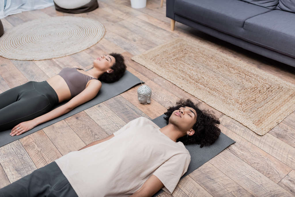 Hoge hoek uitzicht van Afrikaanse Amerikaanse man liggend op yoga mat in de buurt van vriendin en wierook stok - Foto, afbeelding