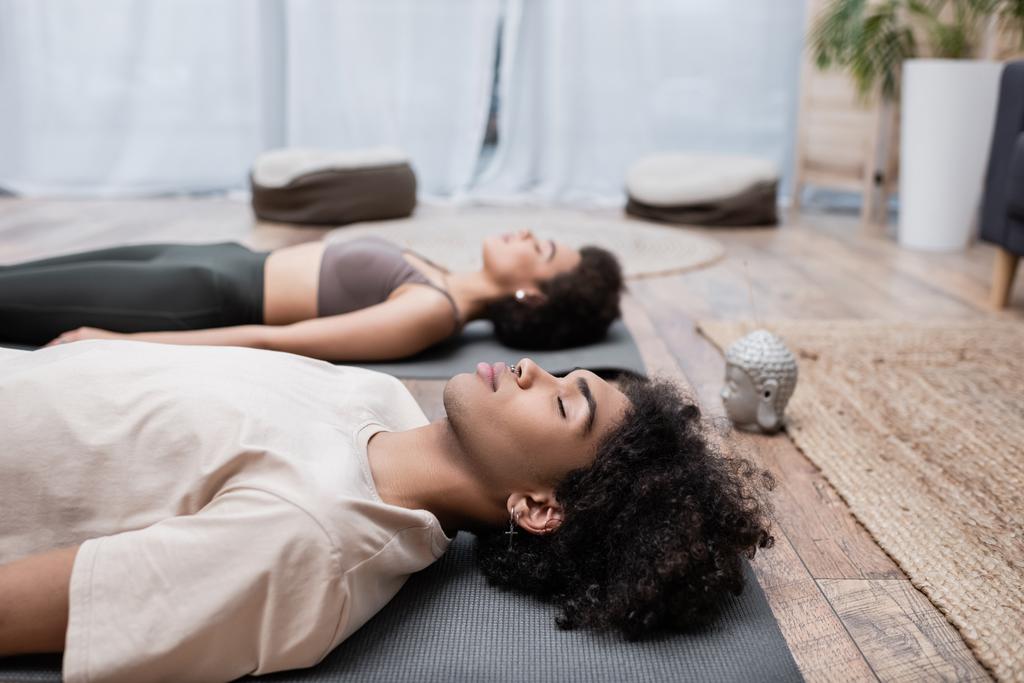 Young african american man meditating near blurred girlfriend on yoga mat at home  - Photo, Image