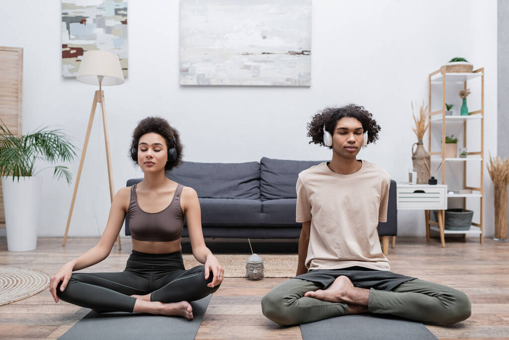 Young african american couple in headphones meditating at home  - Photo, Image