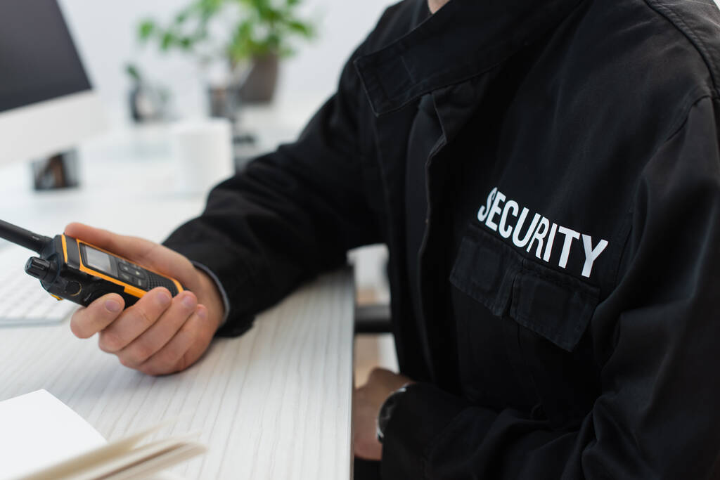 abgeschnittene Ansicht eines Sicherheitsmannes in schwarzer Uniform mit Walkie-Talkie im Büro - Foto, Bild