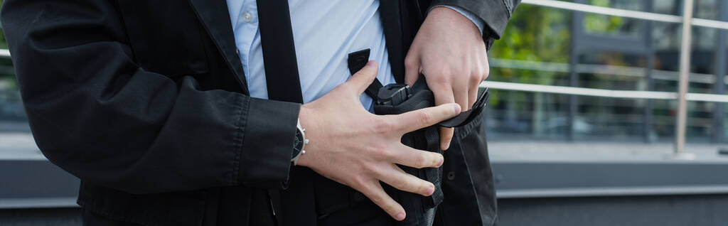 vista parcial del hombre de seguridad sacando el arma de la funda al aire libre, pancarta - Foto, Imagen