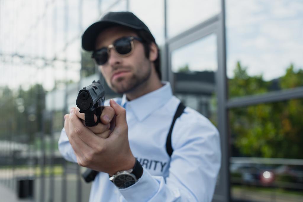 розмитий чоловік безпеки в кепці і сонцезахисних окулярах тримає пістолет на відкритому повітрі
 - Фото, зображення