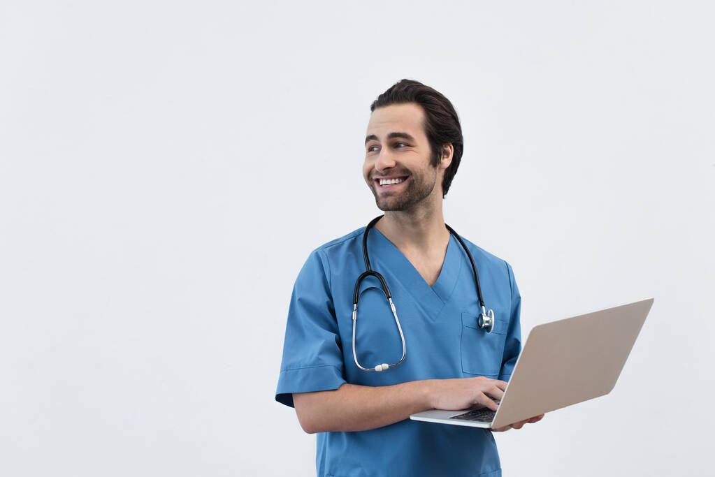 usmívající se lékař s notebookem odvrací pohled izolované na šedé - Fotografie, Obrázek