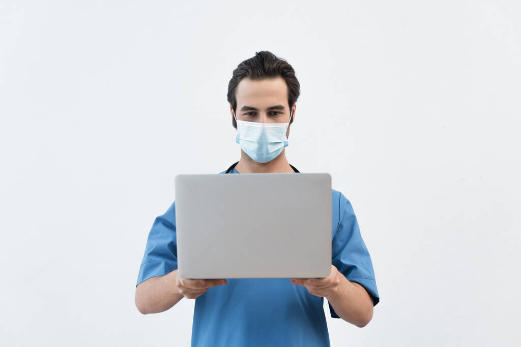 young physician in medical mask holding laptop isolated on grey - Photo, Image