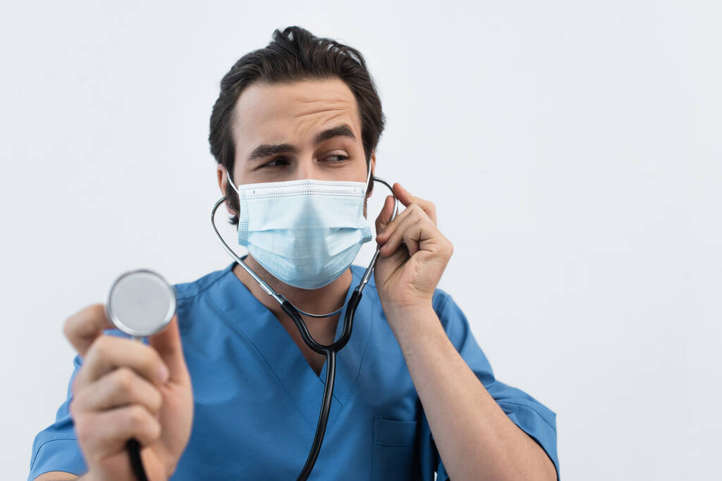 thoughtful doctor in medical mask using stethoscope isolated on grey - Photo, Image