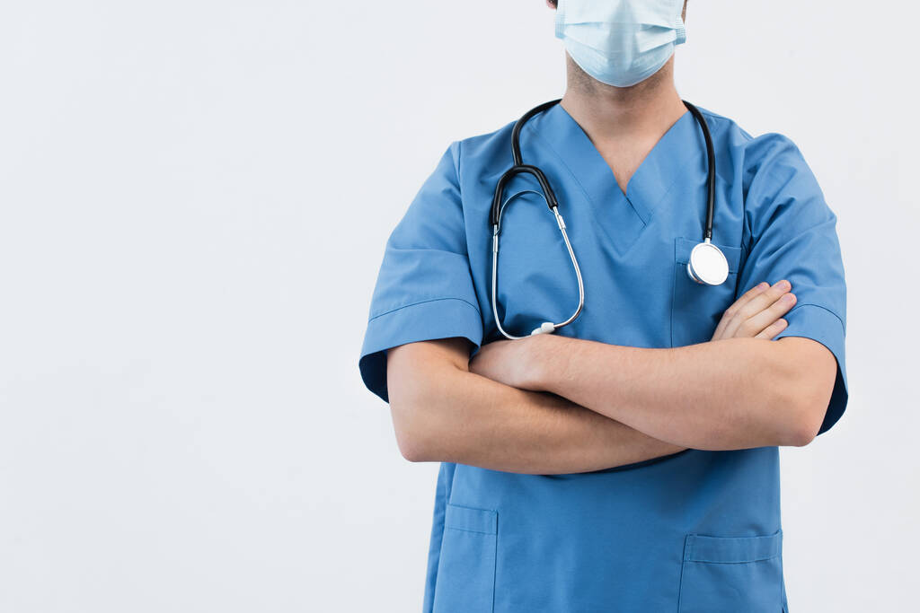 Mavi üniformalı ve tıbbi maskeli doktorun gri kolları çapraz duruş görüntüsü. - Fotoğraf, Görsel