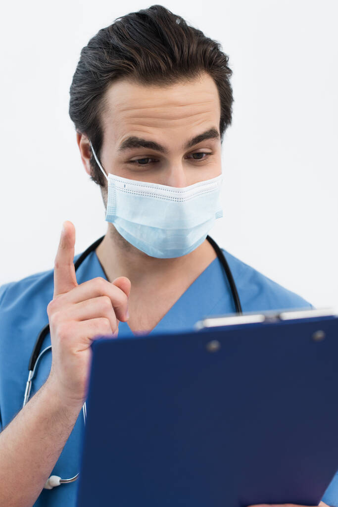 lekarz w masce medycznej pokazuje gest idei w pobliżu rozmazanego schowka odizolowanego na szaro - Zdjęcie, obraz