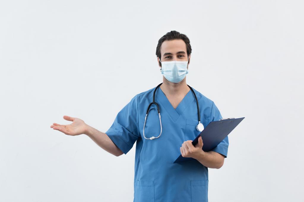 arts in medisch masker houden klembord en wijzen met de hand geïsoleerd op grijs - Foto, afbeelding