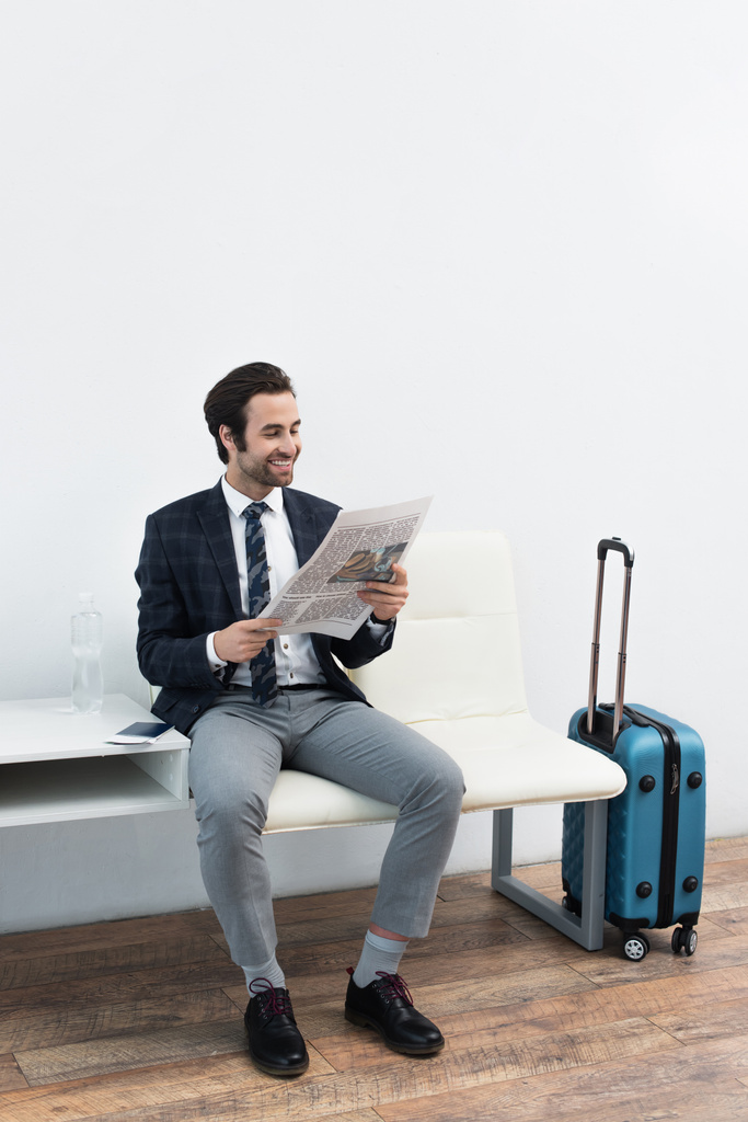 uomo sorridente che legge il giornale vicino alla borsa da viaggio nella sala partenze - Foto, immagini