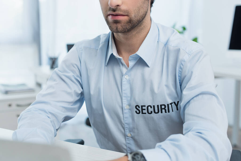 vista recortada del hombre de seguridad que trabaja en la computadora portátil borrosa en la oficina - Foto, imagen