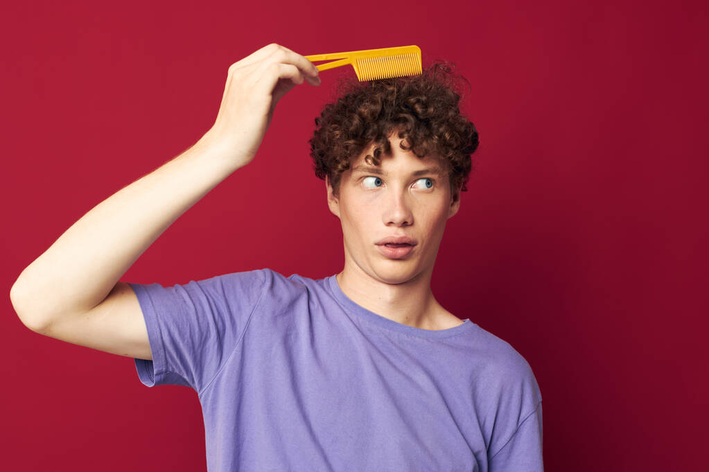 portrait of a young curly man in purple t-shirts with a comb isolated background - Photo, Image