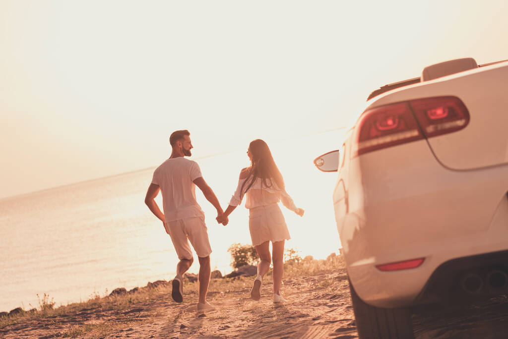 Фото веселих безтурботних подружніх пар, одягнених в білий одяг за кермом автомобіля, що йде пляж, тримає руки на відкритому повітрі сільська дорога
 - Фото, зображення