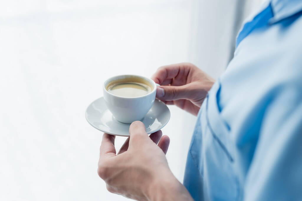 Elinde kahve fincanı olan pijamalı bulanık adamın kısmi görüntüsü. - Fotoğraf, Görsel