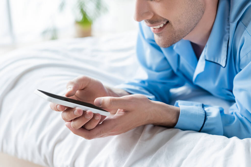 vágott kilátás mosolygós férfi üzenetküldés mobiltelefon az ágyban - Fotó, kép