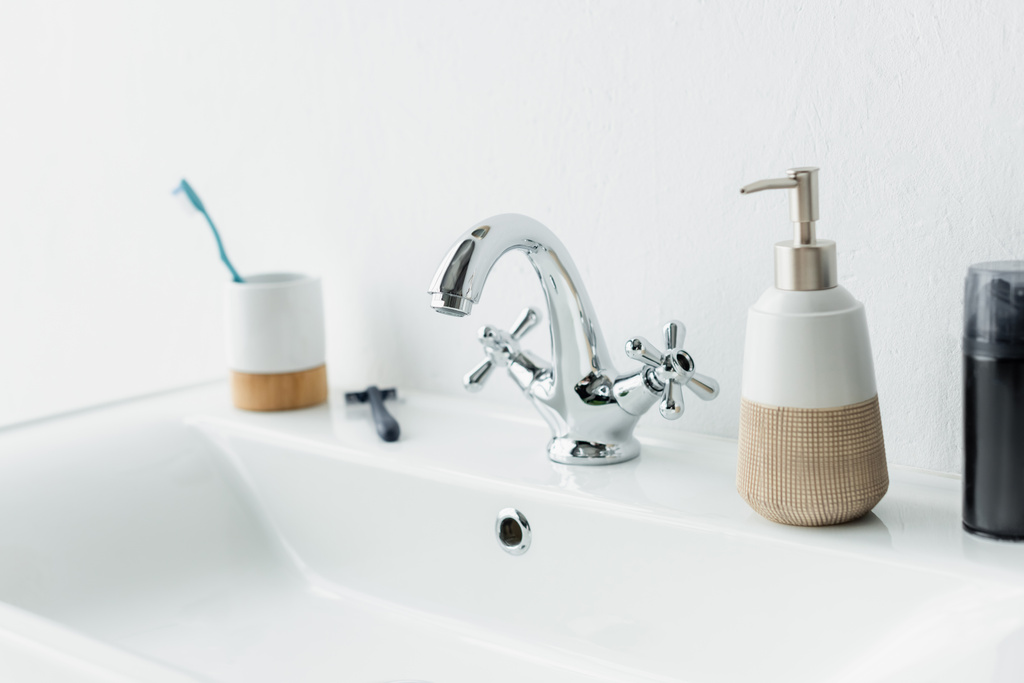 Rasierschaum, Flüssigseife, Sicherheitsrasierer und Zahnbürste auf weißem Waschbecken mit Wasserhahn - Foto, Bild