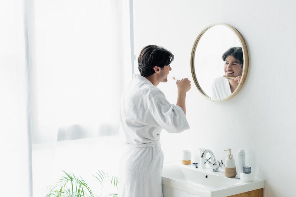 homme souriant brossant les dents près du miroir et évier dans la salle de bain - Photo, image