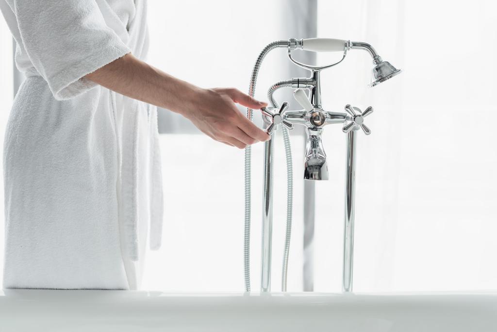 vue partielle de l'homme en peignoir blanc robinet d'ouverture près de la baignoire - Photo, image