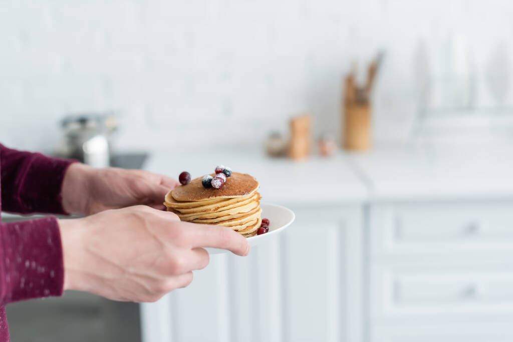 partial view of man holding delicious pancakes with cranberries in blurred kitchen - Photo, Image