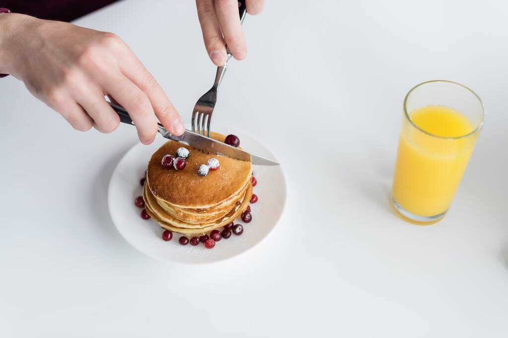 top view of cropped man cutting tasty pancakes near glass of fresh orange juice - Photo, Image