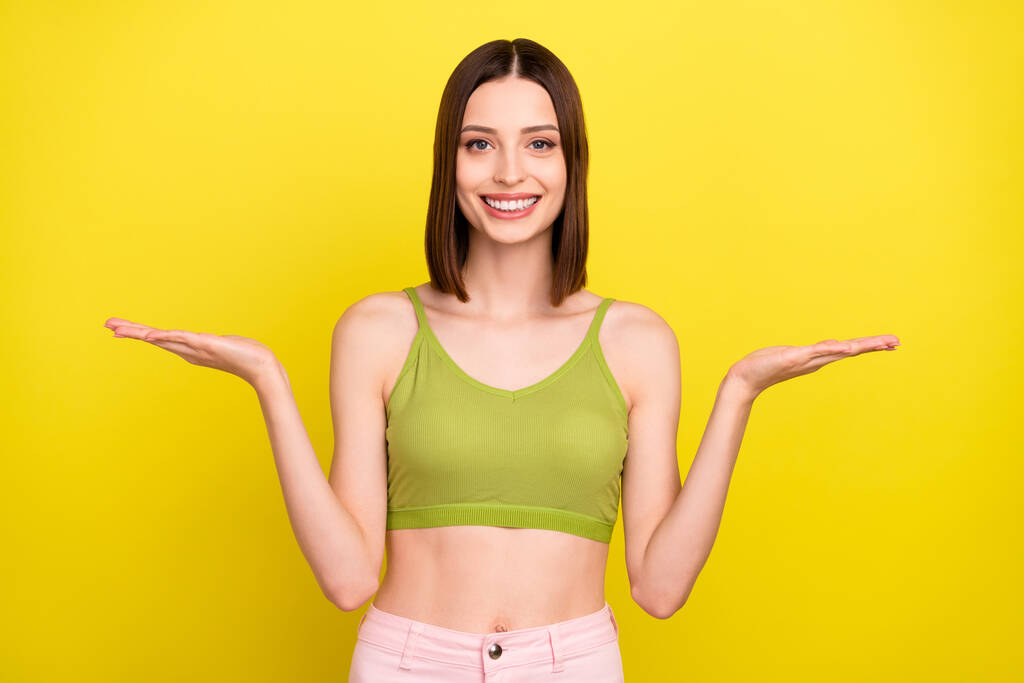 Kuva optimistinen brunette nuori nainen pitää promo kulumista vihreä top farkut eristetty keltainen väri tausta - Valokuva, kuva