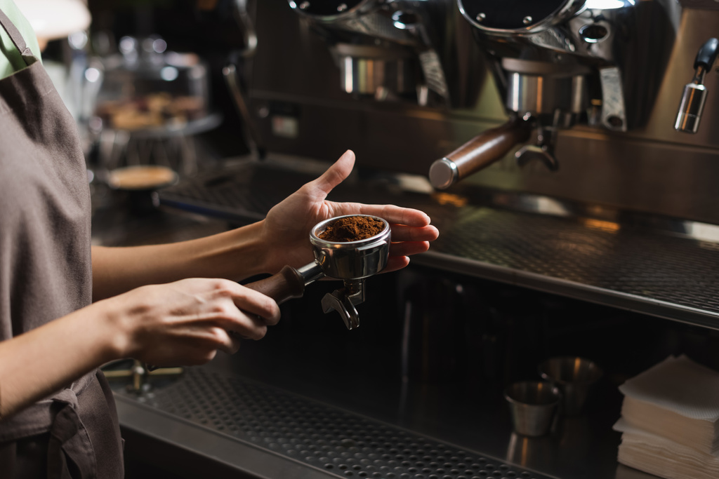 Vista recortada de barista sosteniendo café en portafilter cerca de la máquina de café borrosa en la cafetería  - Foto, Imagen