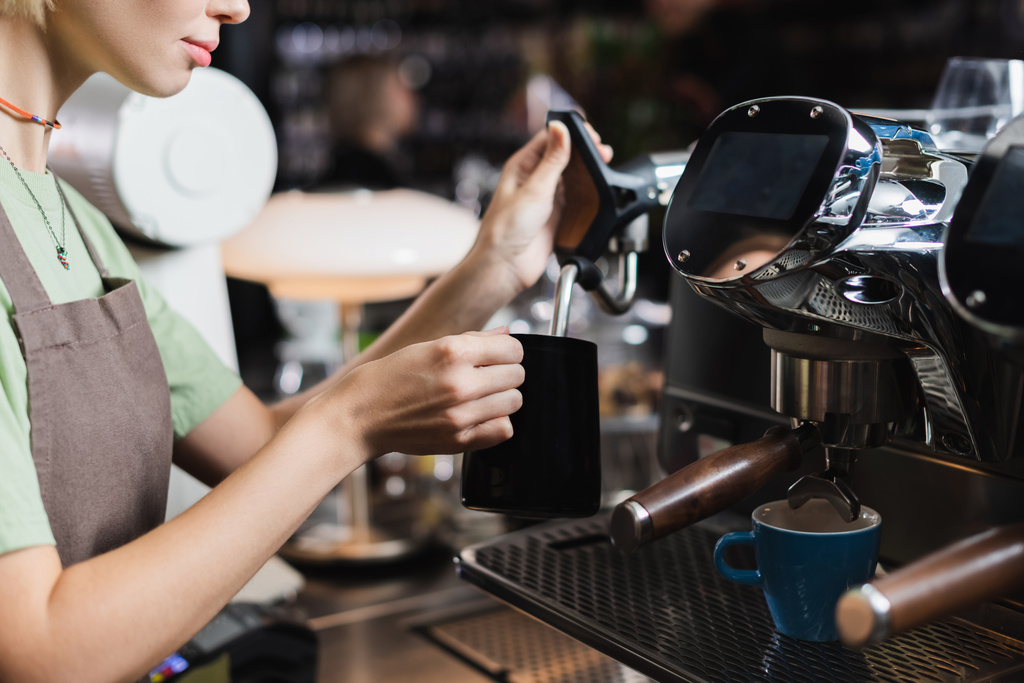 Vágott kilátás fiatal barista dolgozik tejes kancsó és gőzpálca kávéfőző gép kávézóban - Fotó, kép