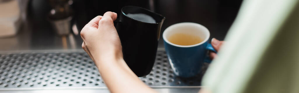 カフェ、バナーでミルクジャグとカップを保持バリスタの作物ビュー  - 写真・画像