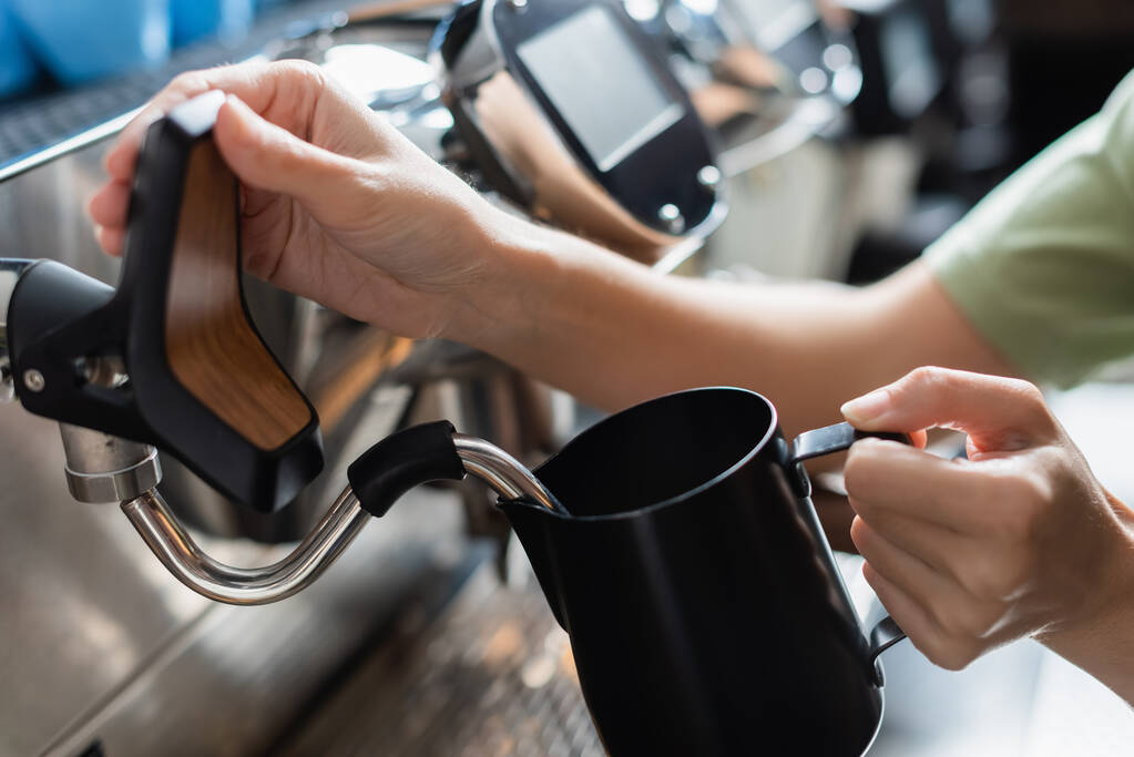 Gewassen uitzicht op barista houden melk kan in de buurt van koffiezetapparaat met stoom toverstokje in cafetaria  - Foto, afbeelding