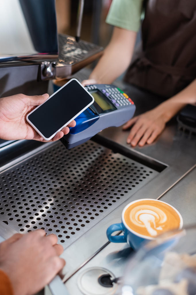 アフリカ系アメリカ人の顧客がバリスタ近くの携帯電話で支払い、カフェでコーヒーを飲む姿を切り取った  - 写真・画像