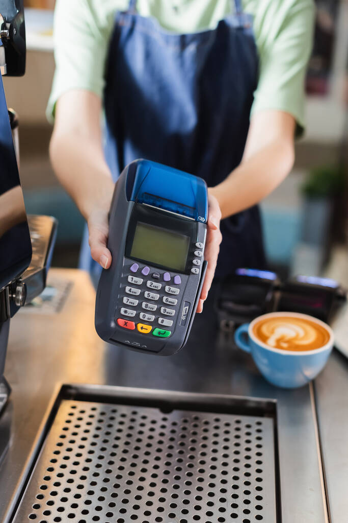 Vista ritagliata del barista offuscata holding terminale di pagamento vicino al caffè in caffè  - Foto, immagini
