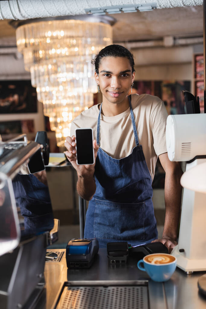 Νεαρός αφρικάνος Αμερικανός barista δείχνει smartphone με λευκή οθόνη κοντά στον καφέ στο καφέ  - Φωτογραφία, εικόνα
